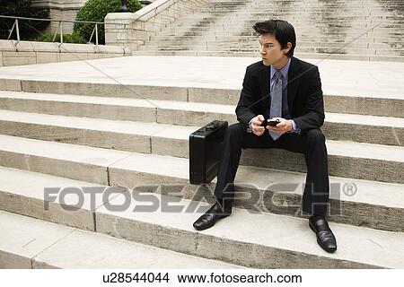 Picture - Asian business man sitting on steps in urban area.. Fotosearch