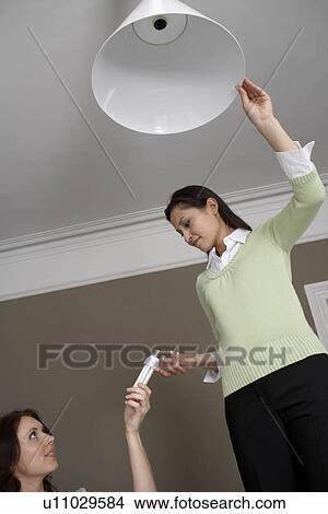 Picture - 2 women changing lightbulb. Fotosearch