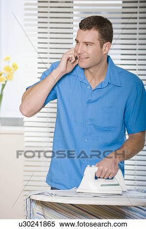 Stock Photography - A male ironing whilst on the phone. Fotosearch