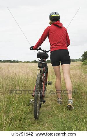 Stock Image - Woman cyclist pushing bicycle rear view. Fotosearch