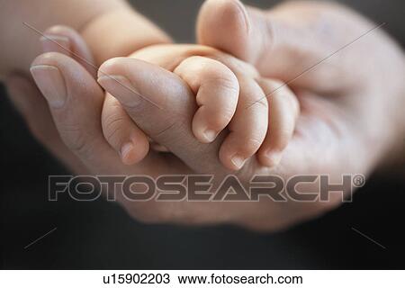 Stock Image - Baby holding man's finger close up of hands. Fotosearch