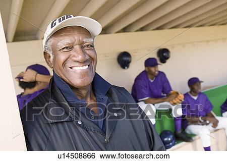 Stock Photograph - Baseball coach in dugout smiling (portrait). Fotosearch