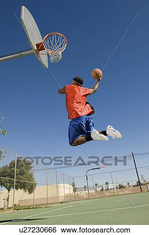 Basketball player mid-air dunking ball side view View Large Photo Image Stock Photograph - Basketball player mid-air dunking ball side view. Fotosearch