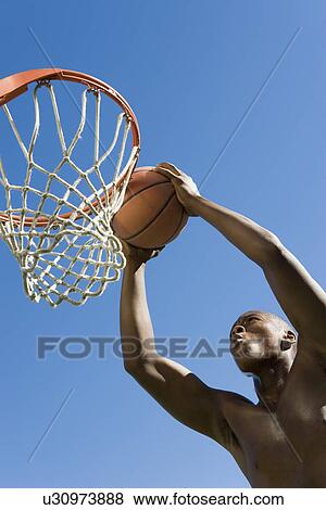 Stock Photo - Basketball player slum dunking ball low angle view. Fotosearch