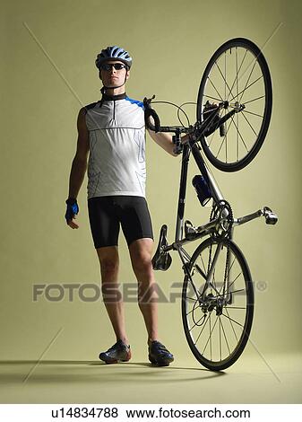 Bicyclist standing holding bicycle on end View Large Photo Image Stock Photo - Bicyclist standing holding bicycle on end. Fotosearch