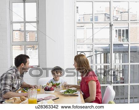 Stock Image - Boy (5-6) eating lunch with parents at dining room table. Fotosearch