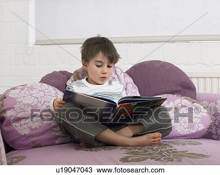 Boy (5-6) reading book on couch in living room View Large Photo Image Stock Image - Boy (5-6) reading book on couch in living room. Fotosearch