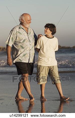 Stock Image - Boy and grandfather walking on beach at dusk. Fotosearch