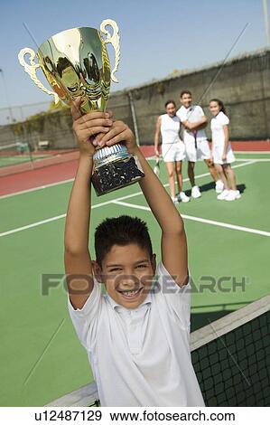 Boy Holding Tennis Trophy at net on tennis court portrait high angle view View Large Photo Image Stock Photo - Boy Holding Tennis Trophy at net on tennis court portrait high angle view. Fotosearch