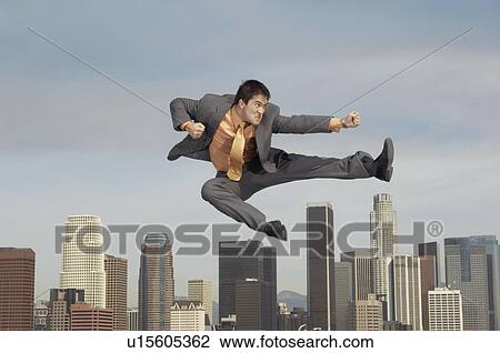 Stock Image - Business man doing martial arts mid-air above city. Fotosearch