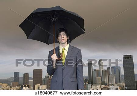 Stock Photo - Business man holding umbrella in city. Fotosearch