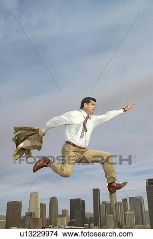 Picture - Business man jumping mid-air above city. Fotosearch