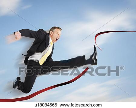 Stock Photography - Business man jumping through red tape digital composite. Fotosearch