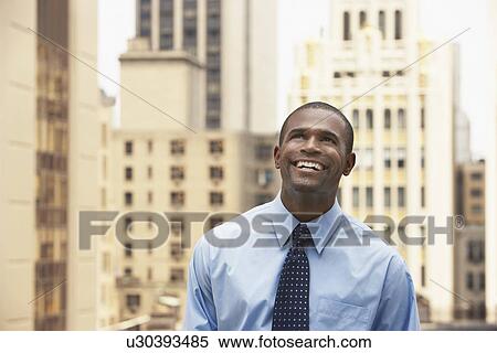 Stock Photography - Business man looking up standing in city half length. Fotosearch