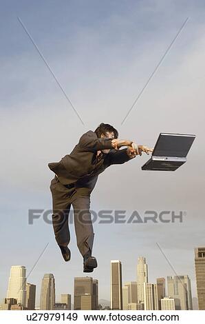 Stock Photo - Business man reaching for laptop mid-air above city. Fotosearch
