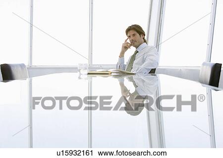 Stock Image - Business man sitting at conference table. Fotosearch