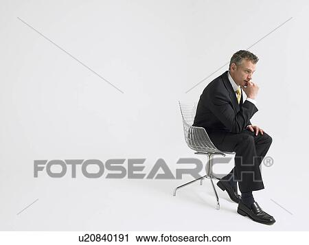 Stock Image - Business man sitting in chair in studio. Fotosearch