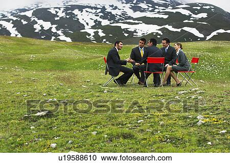 Stock Image - Business People having conference in mountain field. Fotosearch