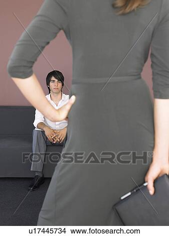 Picture - Business woman back view in front of business man sitting on sofa. Fotosearch
