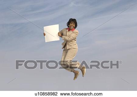 Stock Image - Business woman jumping with blank sign outdoors. Fotosearch