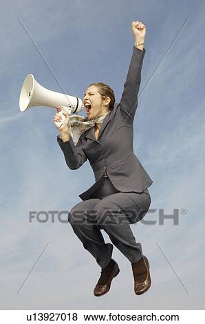 Stock Photo - Business woman shouting in bullhorn mid-air outdoors. Fotosearch