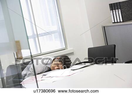 Stock Photograph - Businessman asleep at desk in office by scattered files. Fotosearch