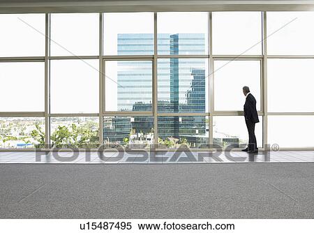 Businessman by window in office building View Large Photo Image Stock Photography - Businessman by window in office building. Fotosearch