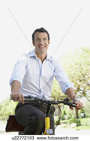 Stock Image - Businessman commuting by bike along tree lined road. Fotosearch
