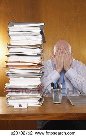 Businessman covering face with hands next to stack of paperwork at desk View Large Photo Image Stock Image - Businessman covering face with hands next to stack of paperwork at desk. Fotosearch