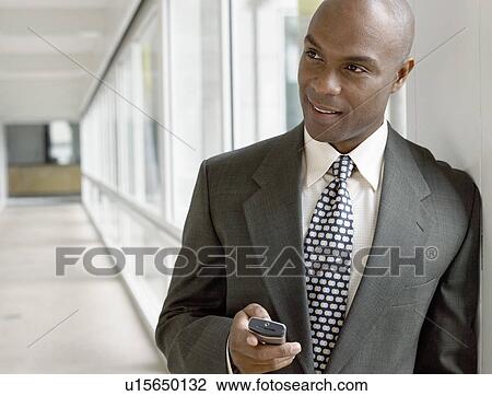 Businessman holding mobile phone in hallway View Large Photo Image Stock Image - Businessman holding mobile phone in hallway. Fotosearch