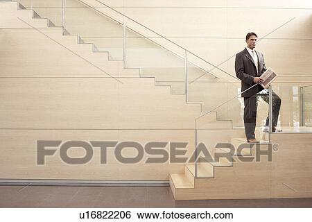 Stock Photograph - Businessman holding newspaper standing on Stairs. Fotosearch