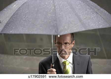 Businessman holding umbrella in front of building elevated view View Large Photo Image Stock Image - Businessman holding umbrella in front of building elevated view. Fotosearch