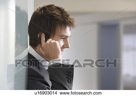 Picture - Businessman in doorway talking on cell phone close up side view. Fotosearch