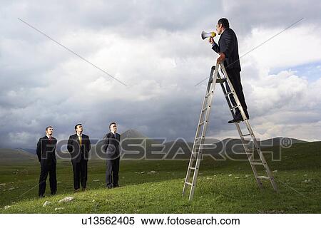 Stock Photography - Businessman in mountain field Speaking Through Megaphone to other businessmen full length. Fotosearch