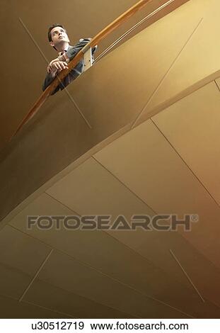 Stock Photo - Businessman leaning on railing of balcony low angle view.. Fotosearch