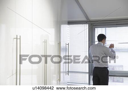Stock Image - Businessman Looking out office Window through Venetian blinds. Fotosearch