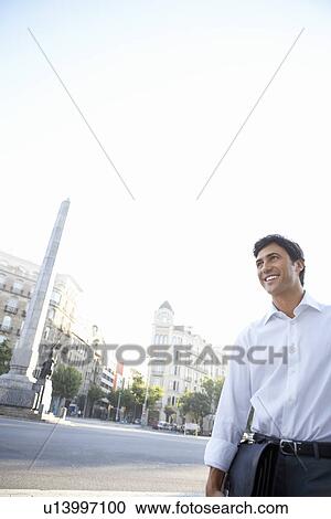 Businessman on city street holding briefcase by high-rise buildings View Large Photo Image Stock Image - Businessman on city street holding briefcase by high-rise buildings. Fotosearch