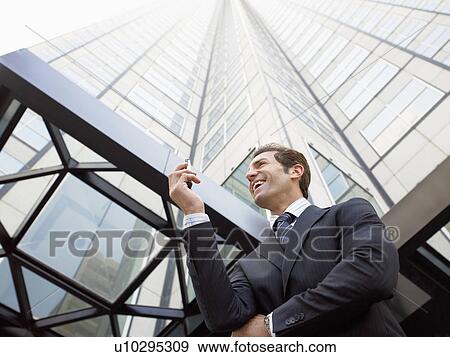 Businessman reading message on phone outside office (low angle view) View Large Photo Image Stock Photo - Businessman reading message on phone outside office (low angle view). Fotosearch