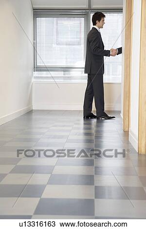 Stock Image - Businessman Shaking Hands through doorway with unseen person side view. Fotosearch