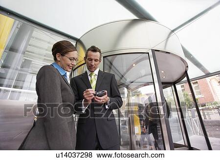 Stock Photo - Businessman showing businesswoman PDA in front of revolving door low-angle view. Fotosearch