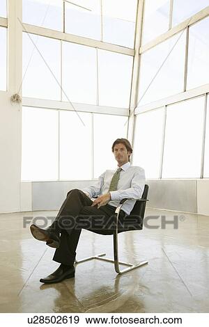 Businessman sits in sunlit office with knees crossed View Large Photo Image Stock Photo - Businessman sits in sunlit office with knees crossed. Fotosearch