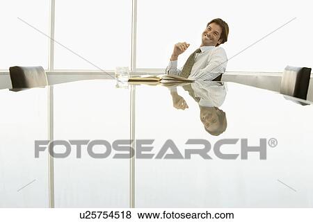 Stock Photo - Businessman sitting at conference table smiling. Fotosearch