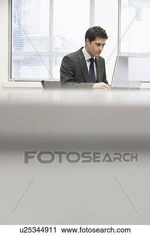 Businessman sitting at desk in office Using Laptop View Large Photo Image Stock Image - Businessman sitting at desk in office Using Laptop. Fotosearch