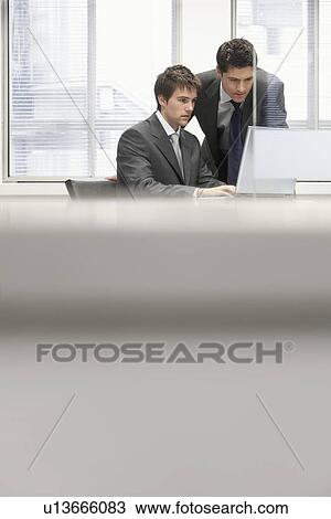 Businessman sitting at office desk showing other businessman work on laptop View Large Photo Image Stock Image - Businessman sitting at office desk showing other businessman work on laptop. Fotosearch