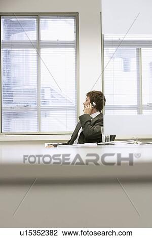 Businessman sitting at office desk Talking on Cell Phone View Large Photo Image Stock Image - Businessman sitting at office desk Talking on Cell Phone. Fotosearch