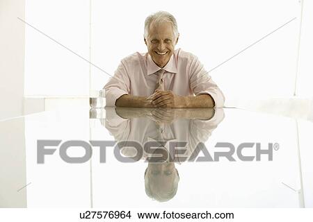 Businessman sitting at table smiling portrait View Large Photo Image Picture - Businessman sitting at table smiling portrait. Fotosearch