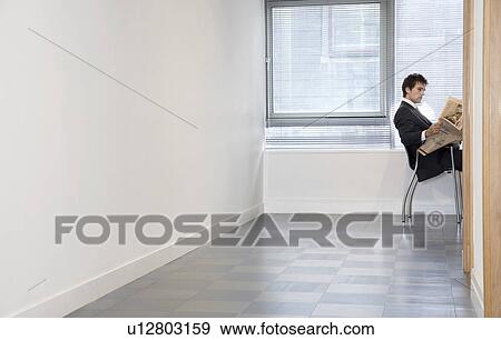 Businessman sitting in empty room reading newspaper side view View Large Photo Image Stock Photo - Businessman sitting in empty room reading newspaper side view. Fotosearch