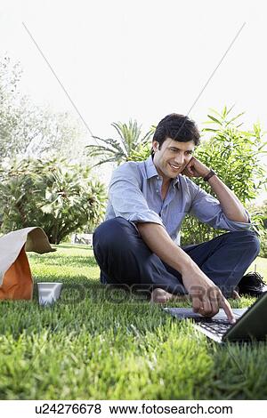 Businessman sitting on grass in park using laptop View Large Photo Image Stock Photo - Businessman sitting on grass in park using laptop. Fotosearch