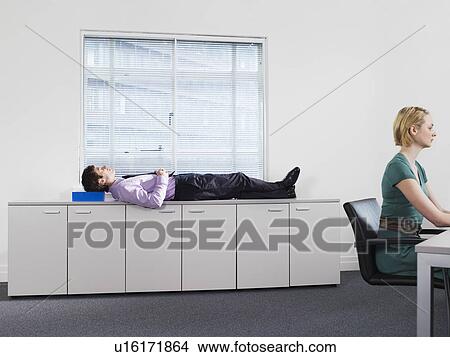 Businessman sleeping on office cabinets near woman working View Large Photo Image Picture - Businessman sleeping on office cabinets near woman working. Fotosearch
