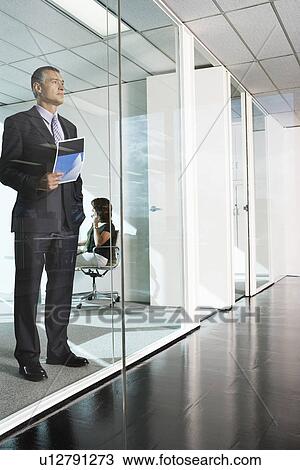Businessman standing behind glass wall in office interior View Large Photo Image Stock Image - Businessman standing behind glass wall in office interior. Fotosearch